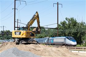 Haines & Kibblehouse, Inc.: A Caterpillar M322F works on I-95 as an Amtrak Acela flies by on the Northeast Corridor. 